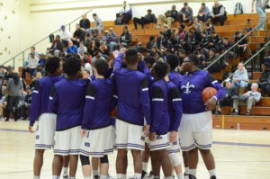 New Rochelle’s basketball team huddles up before their Jan. 21 game against Mount Vernon. Although meetings between the two teams usually lead to packed gyms, postgame violence three weeks ago led the Huguenots to close the gym and turn fans away. Photo/Mike Smith